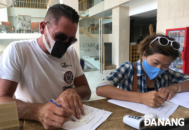 tourists filling out their health declaration forms under the guidance of hotel receptionists